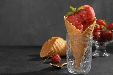 Delicious strawberry ice cream in wafer cone served on black table, space for text
