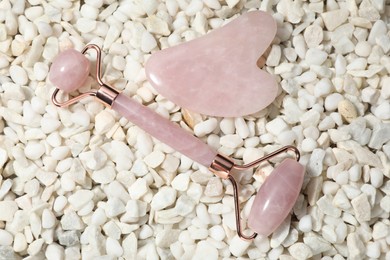 Photo of Quartz gua sha tool and face roller on white stones, flat lay