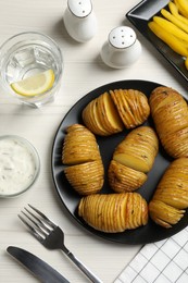 Delicious homemade Hasselback potatoes served on white wooden table, flat lay