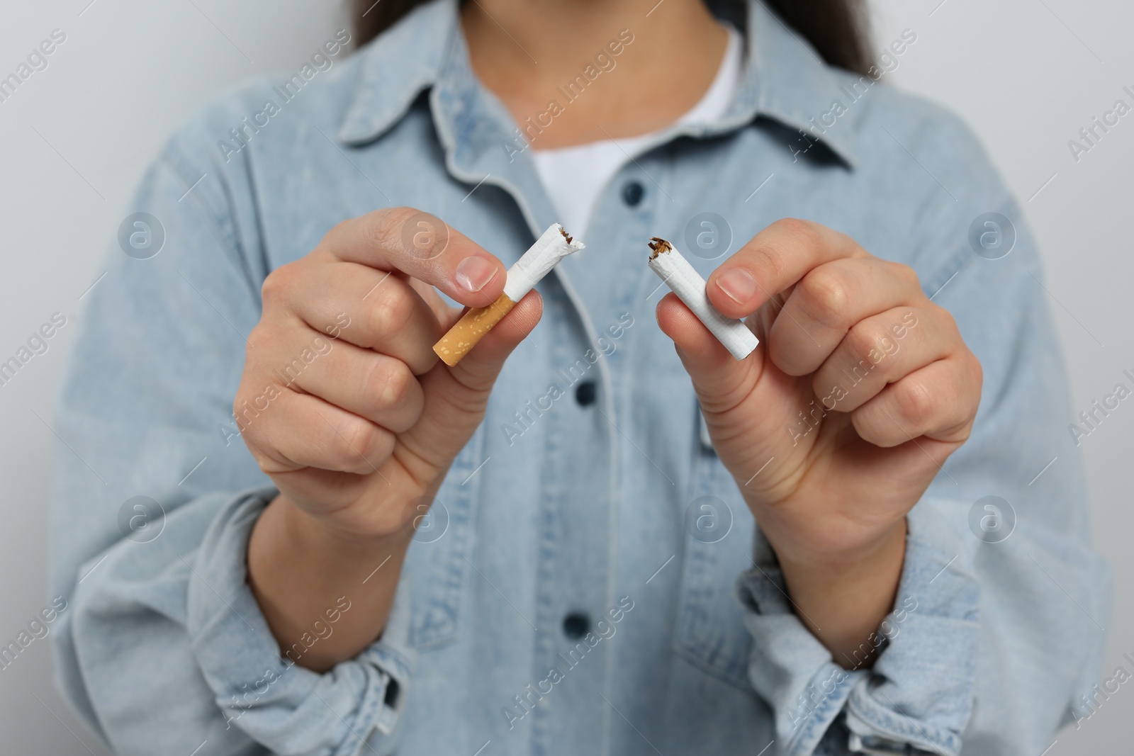 Photo of Stop smoking concept. Woman holding pieces of broken cigarette on light grey background, closeup