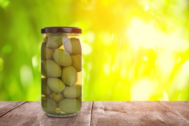 Image of Jar of pickled olives on wooden table against blurred background, space for text
