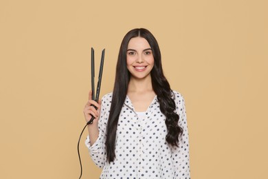 Beautiful happy woman with hair iron on beige background