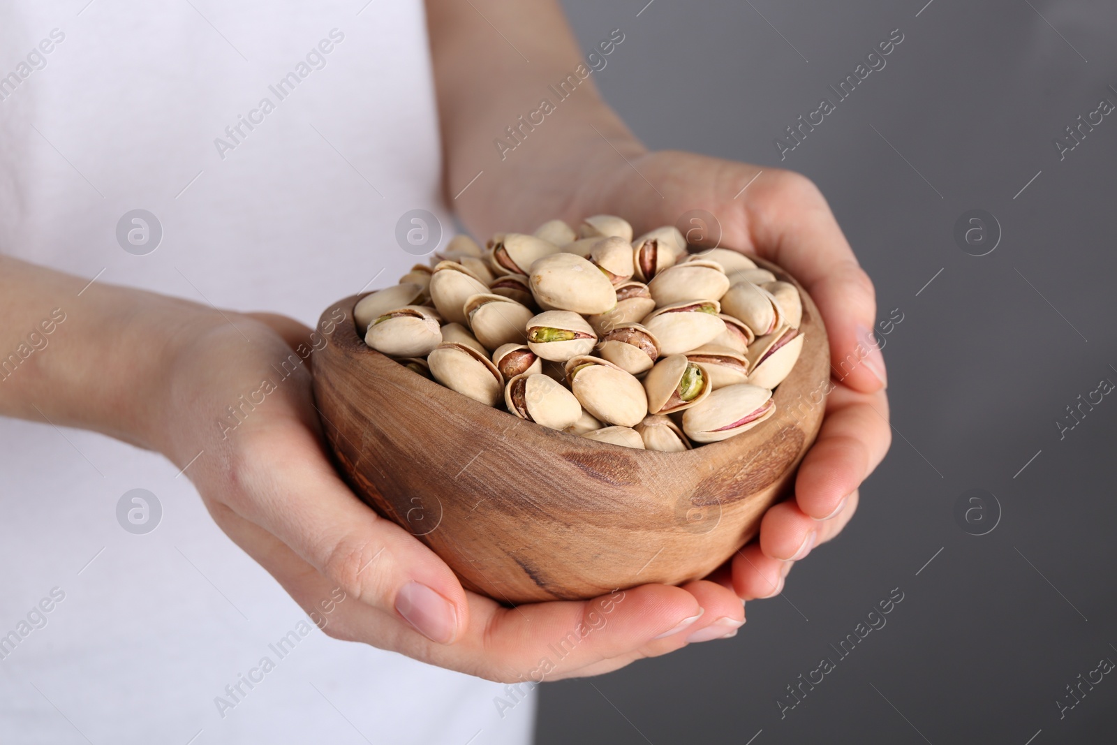 Photo of Woman holding tasty pistachios in bowl on grey background, closeup