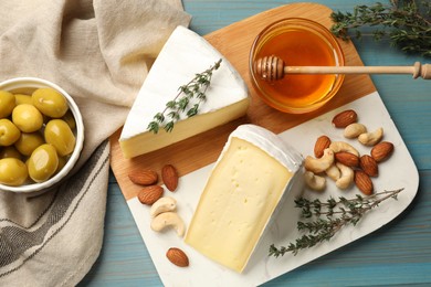 Photo of Tasty Camembert cheese with thyme, honey and nuts on light blue wooden table, flat lay