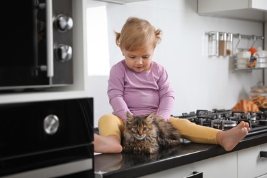 Photo of Cute little child sitting with adorable pet on countertop in kitchen