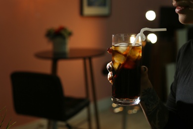 Woman with glass of cold cola in dark cafe, closeup. Space for text