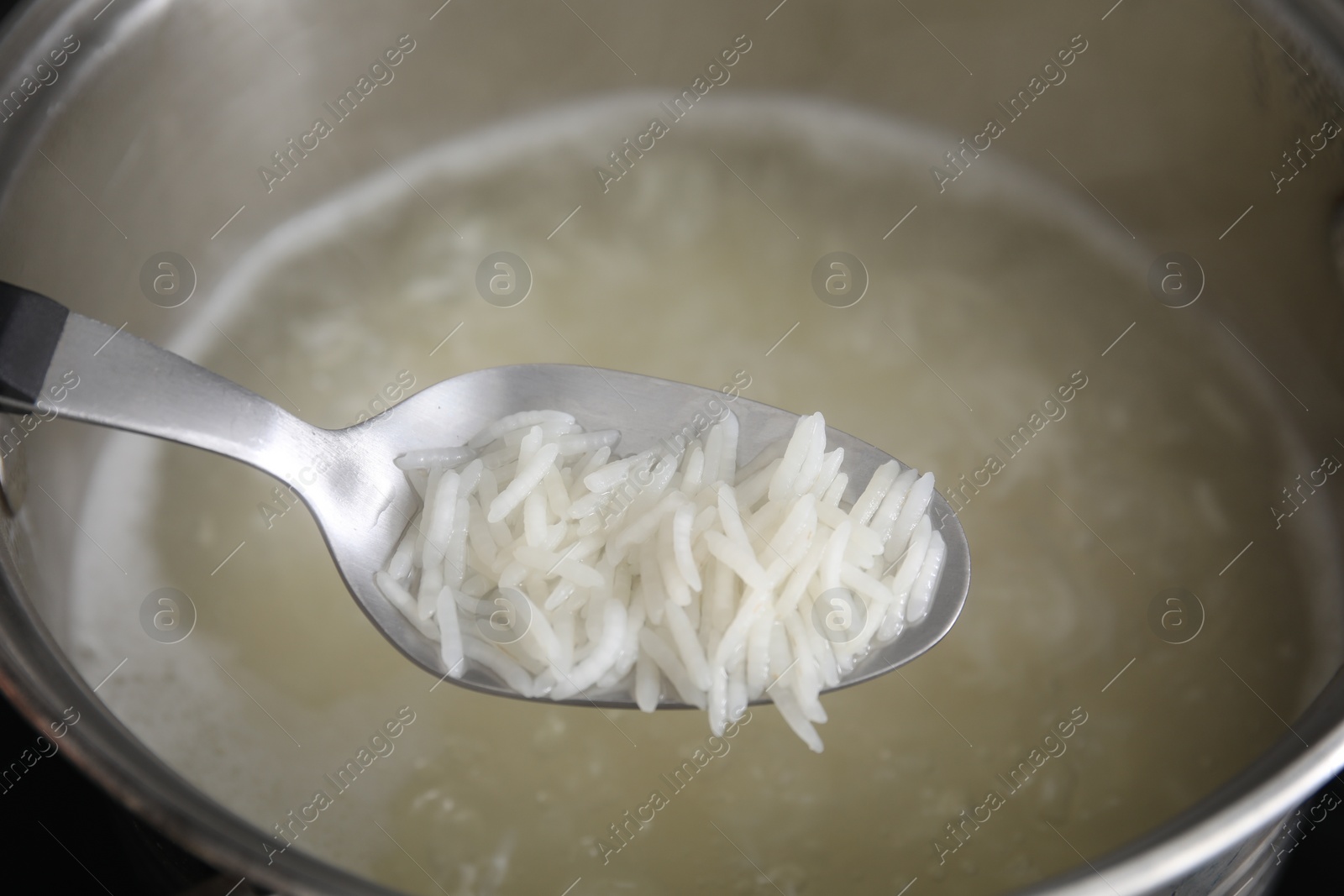 Photo of Spoon with cooked rice over pot, closeup