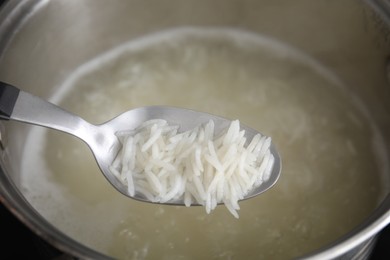 Photo of Spoon with cooked rice over pot, closeup