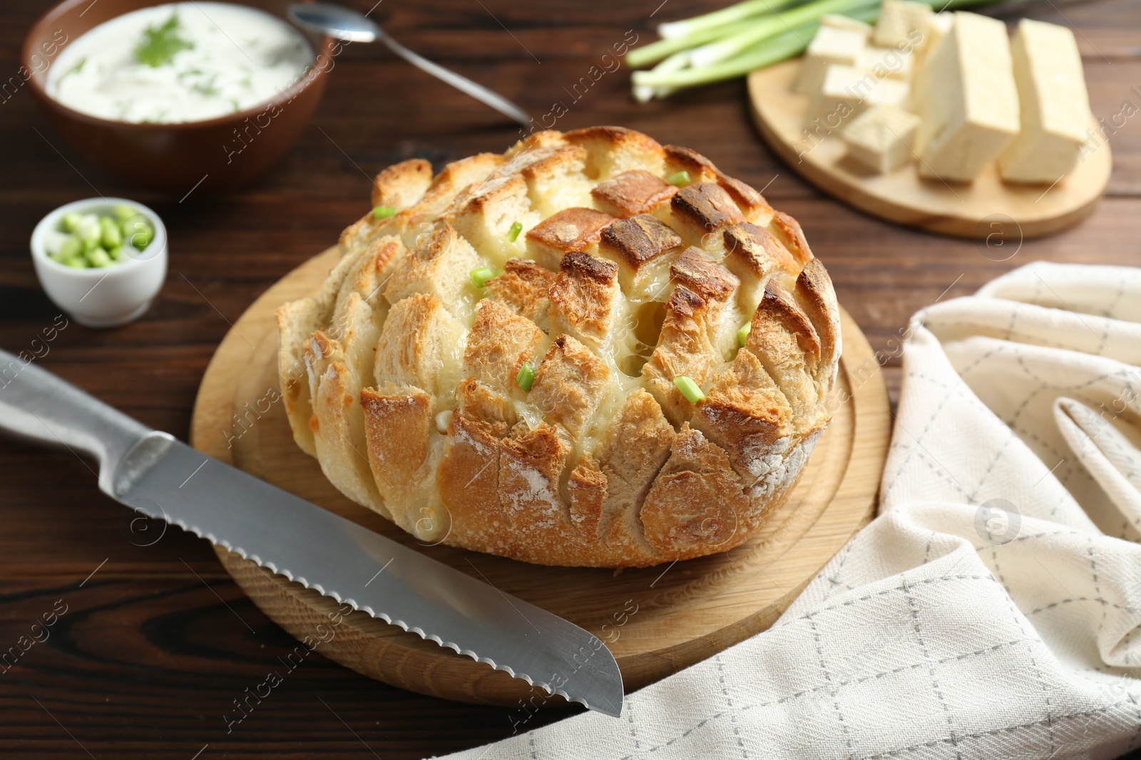 Photo of Freshly baked bread with tofu cheese, green onions, sauce and knife on wooden table