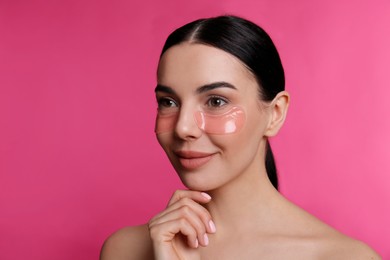 Beautiful young woman with under eye patches on pink background