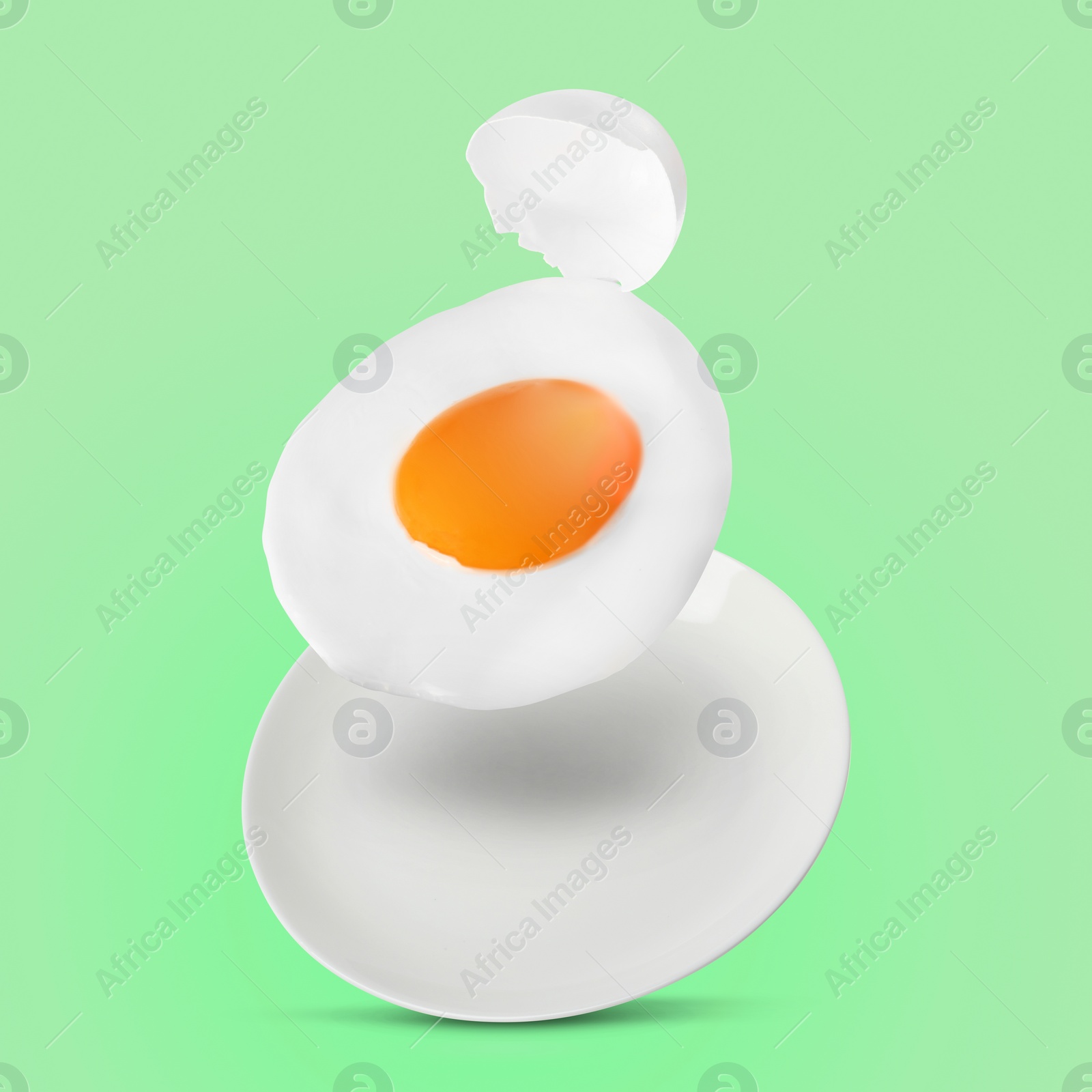 Image of Tasty fried chicken egg with shell falling into plate on color background