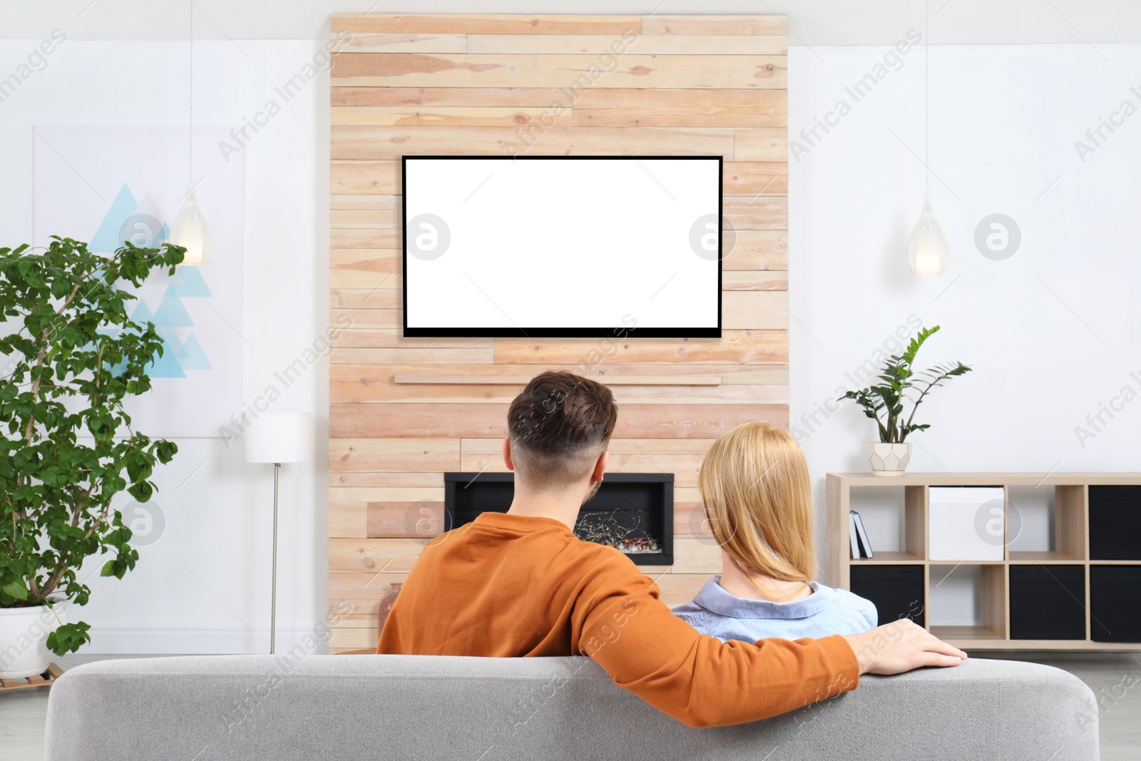 Photo of Couple watching TV on sofa in living room with decorative fireplace