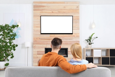 Photo of Couple watching TV on sofa in living room with decorative fireplace