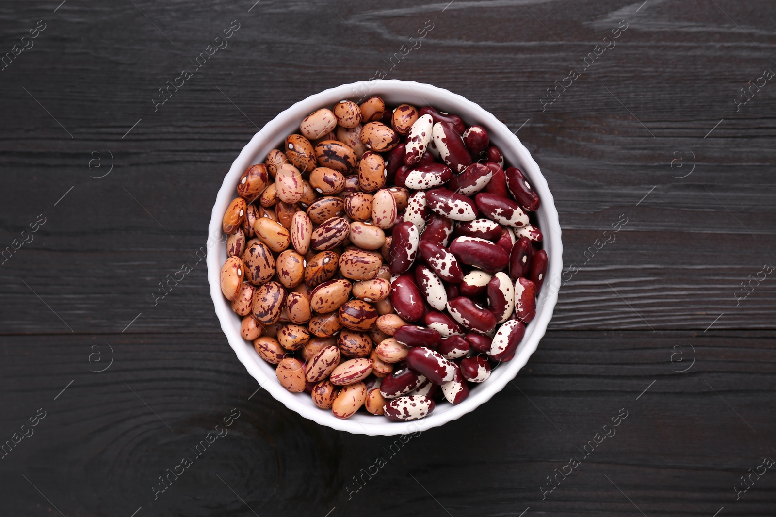 Photo of Different kinds of dry kidney beans in bowl on wooden table, top view