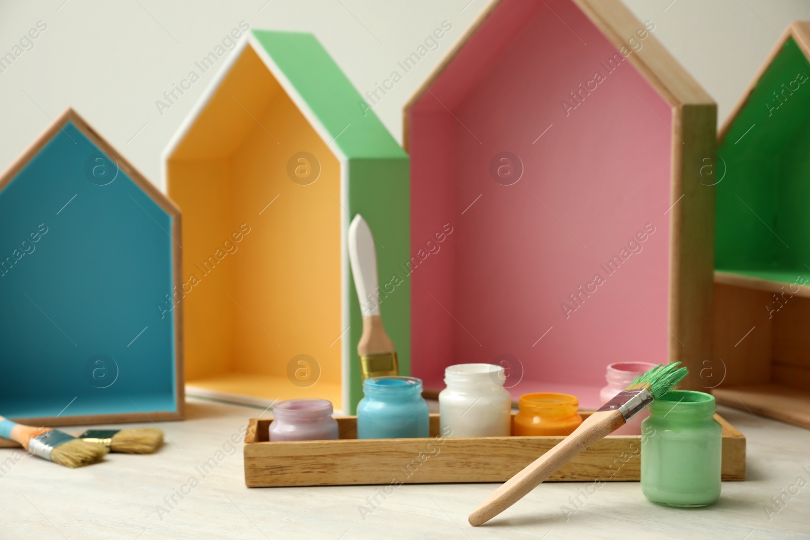 Photo of House shaped shelves, jars of paints and brushes on white table. Interior elements