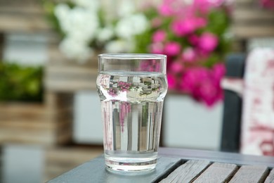 Photo of Glass of fresh water on wooden table outdoors, closeup