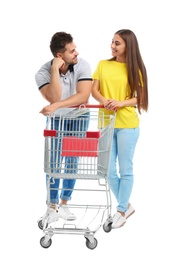 Photo of Young couple with empty shopping cart on white background