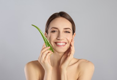 Photo of Happy young woman with aloe leaf on light grey background