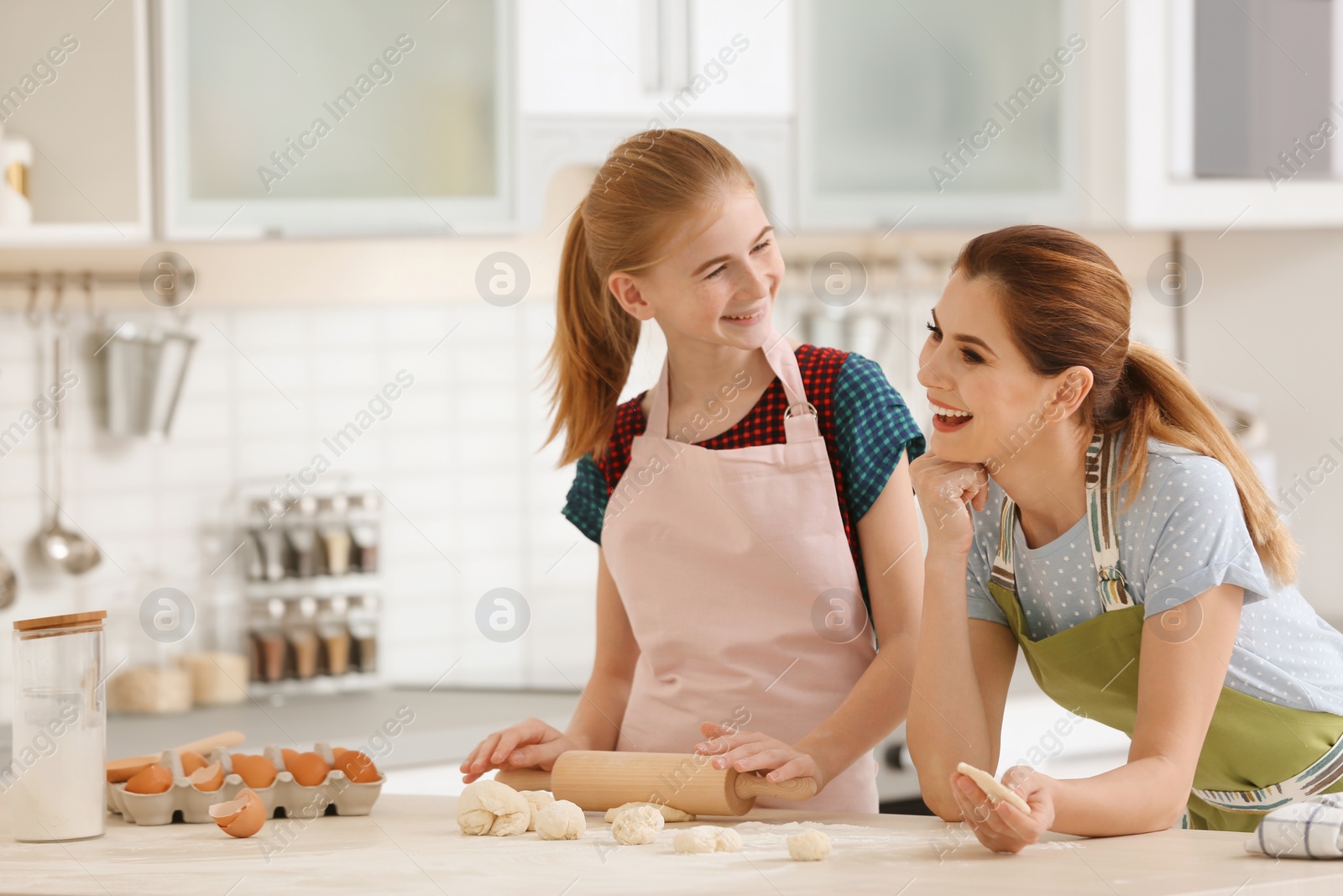 Photo of Mother and her daughter making dough at table in kitchen