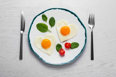 Heart shaped fried eggs served on white wooden table, flat lay