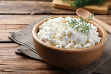 Photo of Fresh cottage cheese with dill in bowl on wooden table, closeup