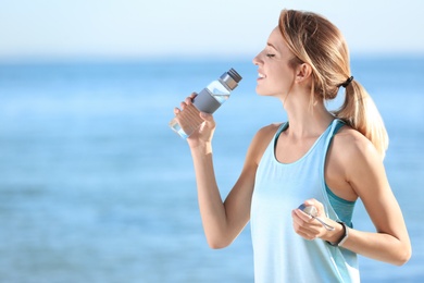 Photo of Young woman drinking water from bottle after fitness exercises on beach in morning