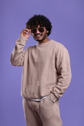 Photo of Handsome smiling man in sunglasses on violet background