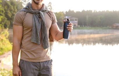 Photo of Young man drinking water on shore of beautiful lake. Camping season
