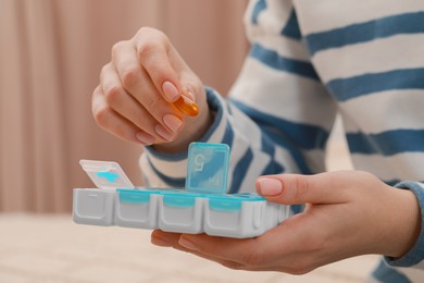 Woman taking pill from plastic box at home, closeup