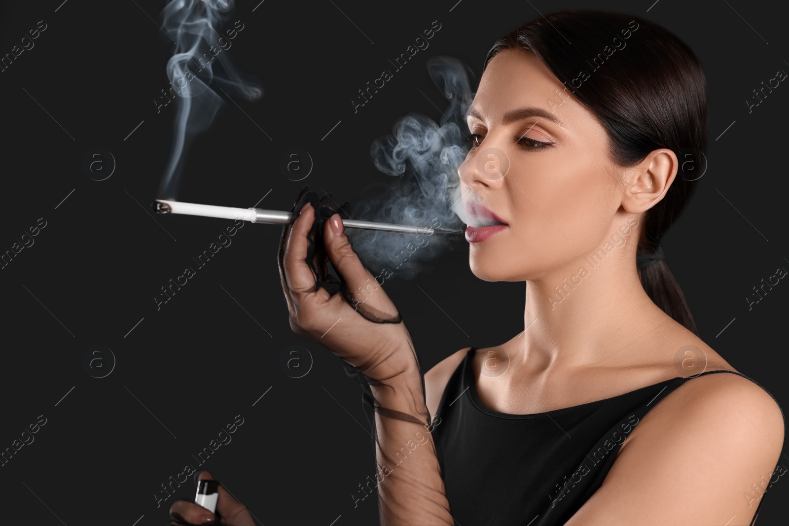 Photo of Woman using long cigarette holder for smoking on black background