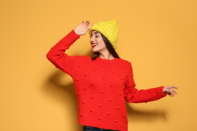 Young woman in warm sweater and knitted hat on color background. Celebrating Christmas