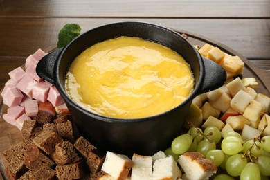 Photo of Fondue pot with melted cheese and different products on wooden table, closeup