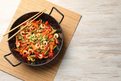 Shrimp stir fry with vegetables in wok and chopsticks on wooden table, top view. Space for text