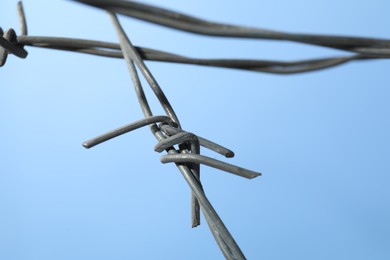 Photo of Metal barbed wire on light blue background, closeup