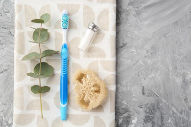 Photo of Plastic toothbrush, eucalyptus branch and other toiletries on grey textured table, top view. Space for text