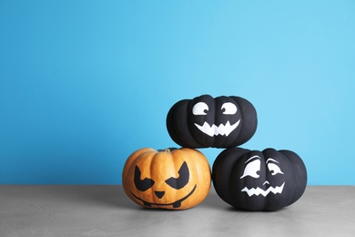 Photo of Pumpkins with scary faces on table against color background, space for text. Halloween decor