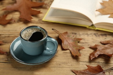 Cup of hot coffee, book and autumn leaves on wooden table, space for text