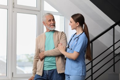 Photo of Young healthcare worker assisting senior man on stairs indoors