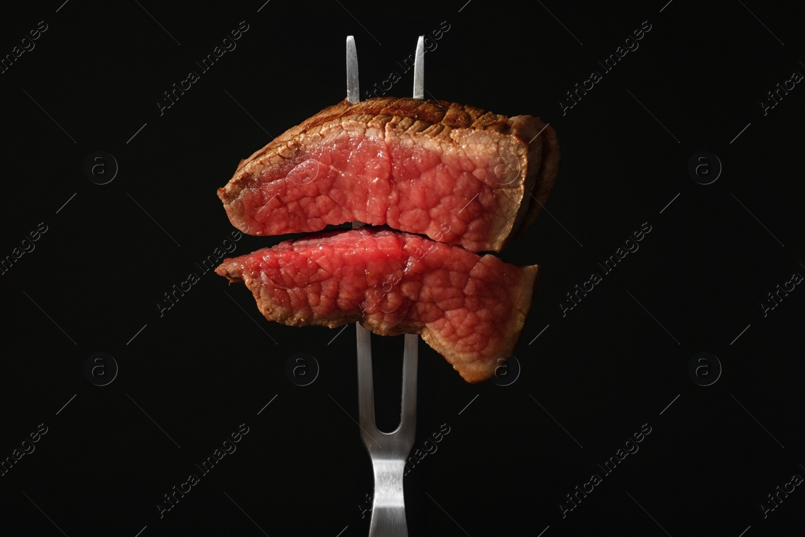 Photo of Carving fork with pieces of steak on black background. Tasty meat