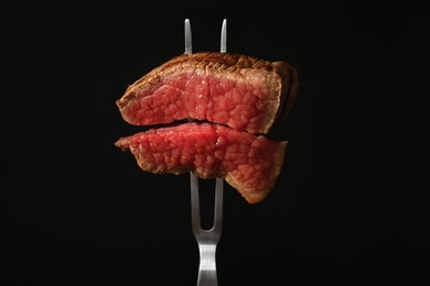 Photo of Carving fork with pieces of steak on black background. Tasty meat
