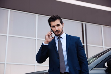 Attractive young man talking on phone near luxury car outdoors
