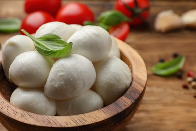 Photo of Delicious mozzarella balls and basil in bowl on wooden table, closeup