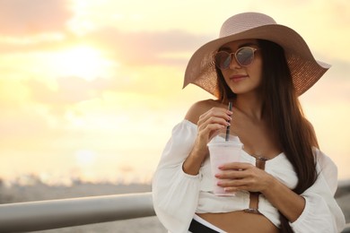 Photo of Beautiful young woman with tasty milk shake outdoors, space for text