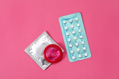 Contraception choice. Pills and condoms on magenta background, flat lay