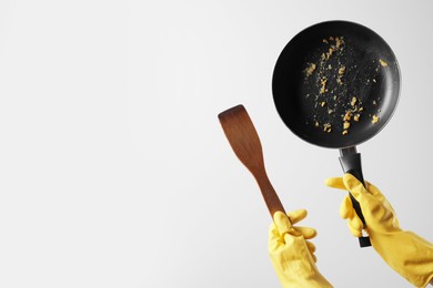 Photo of Woman holding dirty frying pan and spatula on white background, closeup. Space for text