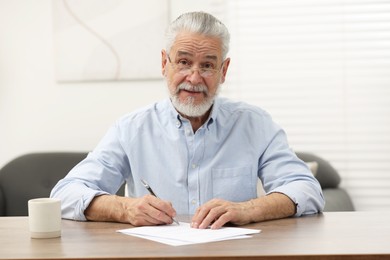 Senior man signing Last Will and Testament at wooden table indoors