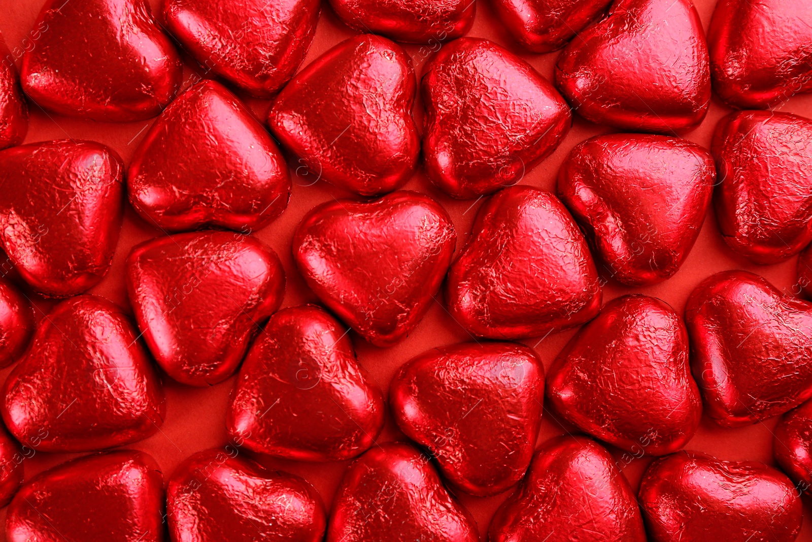 Photo of Heart shaped chocolate candies on red background, flat lay