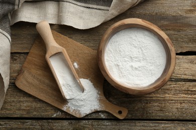 Photo of Baking powder in bowl and scoop on wooden table, flat lay