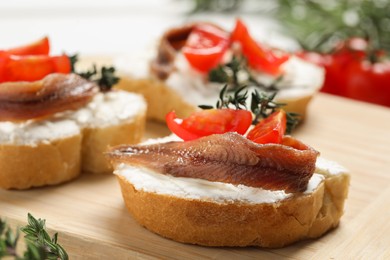 Delicious sandwiches with cream cheese, anchovies and tomatoes on wooden board, closeup