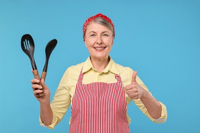 Happy housewife with spoons on light blue background